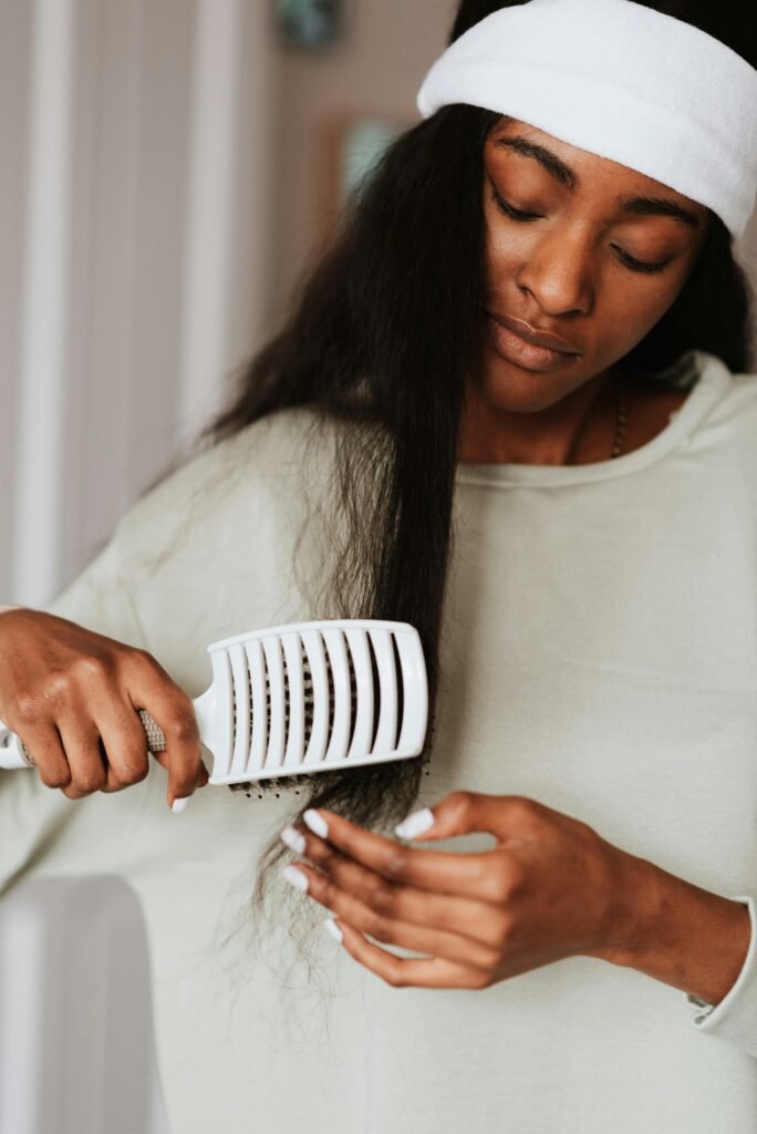 Crop tender ethnic female in headband combing dark hair with brush in house on blurred background